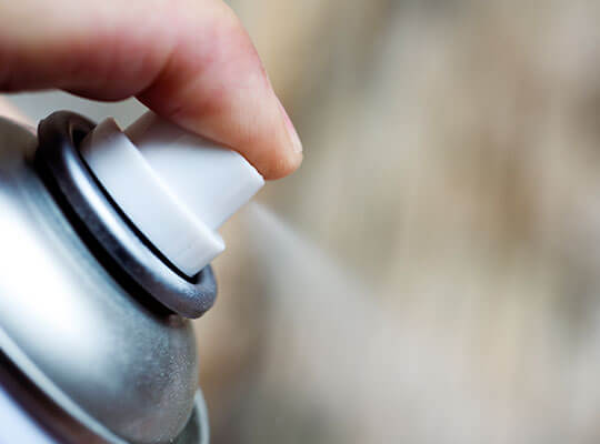 A close up of a man's hand spraying aerosol spray.