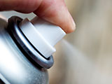 A close up of a man's hand spraying aerosol spray.