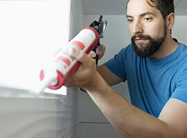 Un hombre sellando una ventana interior.