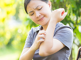 A young woman scratching her arm outside from a mosquito bite.