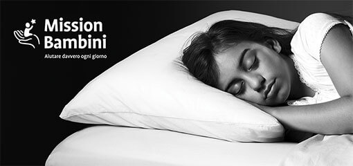 A young girl asleep in bed. This image has a Mission Bambini logo.
